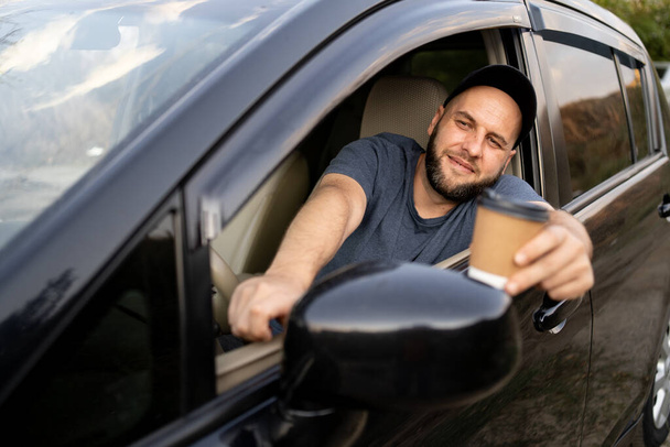 Fröhliche männliche Fahrer mit einer Einwegbecher Kaffee während der Fahrt in einem Auto Blick in den Spiegel. Kopierraum - Foto, Bild