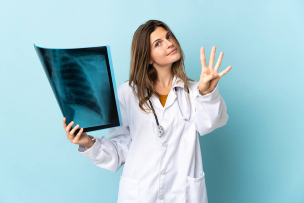 Mladý lékař žena drží radiografii přes izolované pozadí šťastný a počítání čtyři s prsty - Fotografie, Obrázek