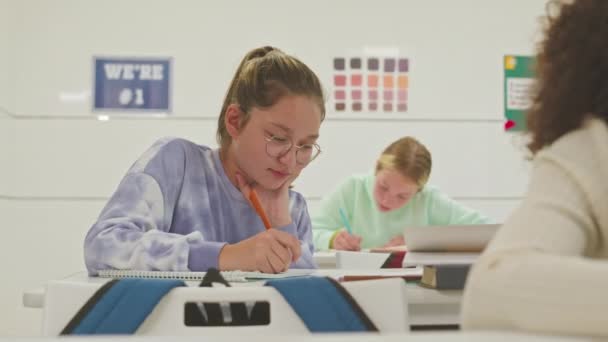 taille tot van Kaukasisch tiener schoolmeisje doen les opdracht terwijl zitten aan wit bureau in modern klaslokaal - Video
