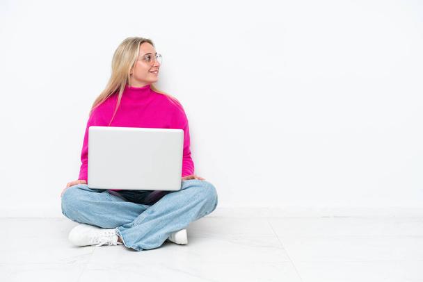 Молодая белая женщина с ноутбуком, сидящая на полу и смотрящая в сторону - Фото, изображение