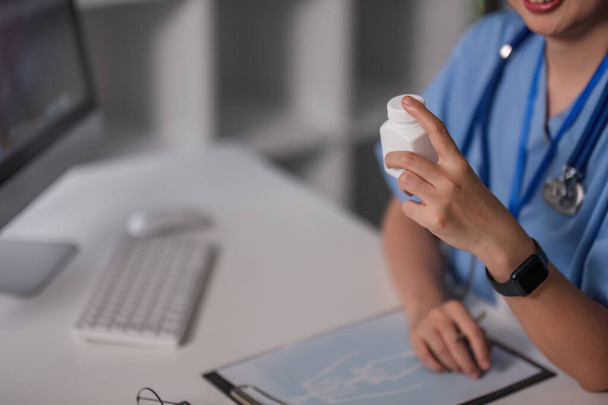 Mano del farmacéutico sosteniendo el frasco de píldoras de plástico mientras se lo muestra a uno de los pacientes durante la consulta en línea. - Foto, imagen