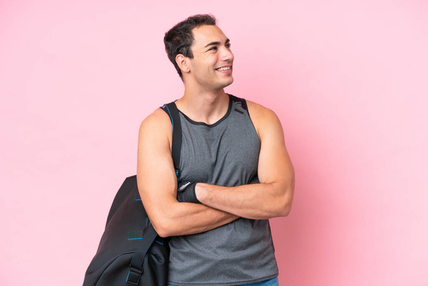 Jonge sport blanke man met sporttas geïsoleerd op roze achtergrond gelukkig en glimlachend - Foto, afbeelding