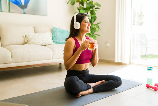 Rahatlamış, sağlıklı bir yaşam tarzı olan güzel bir kadın evde yoga yaparken rehberli bir farkındalık meditasyonunu dinliyor. - Fotoğraf, Görsel