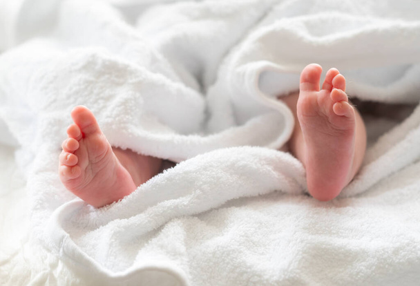 Los infantes pequeños pies que emergen de debajo de la protección reconfortante de una toalla blanca que muestra el cuidado post baño - Foto, imagen