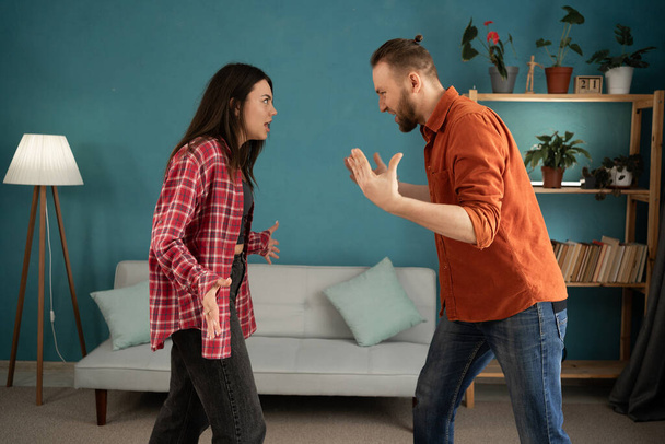 Νεαρό ζευγάρι μαλώνει και τσακώνεται στο σπίτι. Ενδοοικογενειακή βία και σκηνή συναισθηματικής κακοποίησης γυναίκας και άντρα να ουρλιάζουν ο ένας στον άλλο στο σαλόνι. Αντιγραφή χώρου - Φωτογραφία, εικόνα