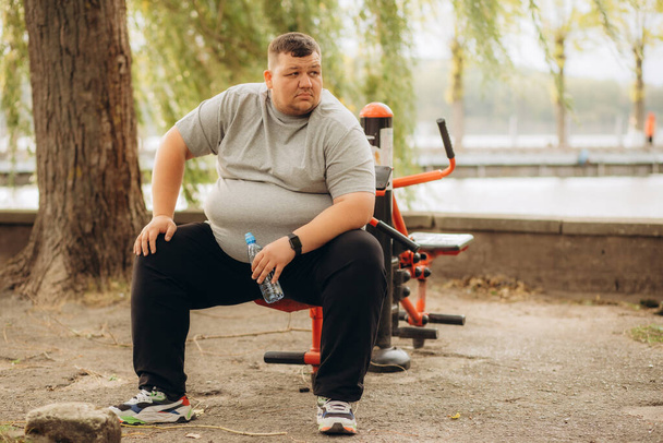 Один втомлений молодий надмірна вага чоловік сидить на лавці парку, щоб відпочити. Товста людина відпочиває на відкритому повітрі. Високоякісна фотографія - Фото, зображення