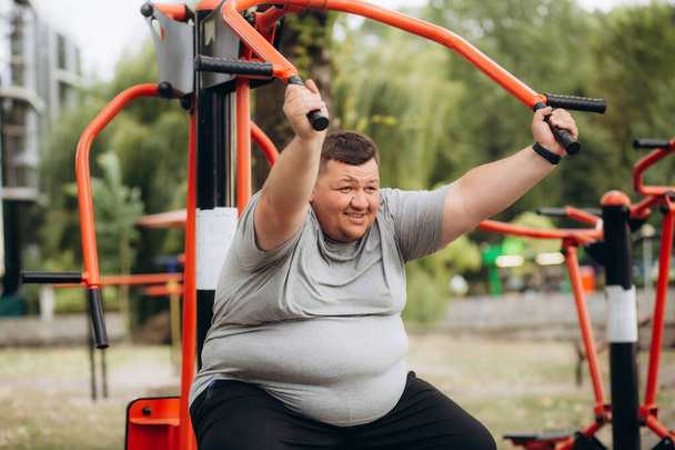 a fat man does sports outdoors on exercise machines - Photo, Image