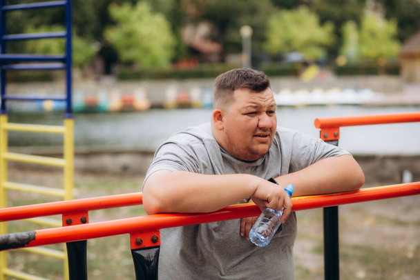 公園で運動した後,ハンバーガーや飲料水を食べる太った男 - 写真・画像