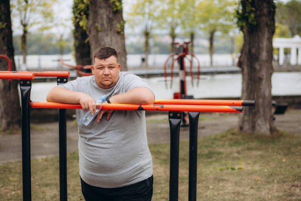 very fat guy drinks water after training in the park in summer. High quality photo - Photo, Image