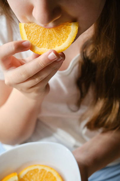 Een meisje eet een sinaasappelschijfje, close-up, zonder ogen. Vitamine voeding, fruit - Foto, afbeelding