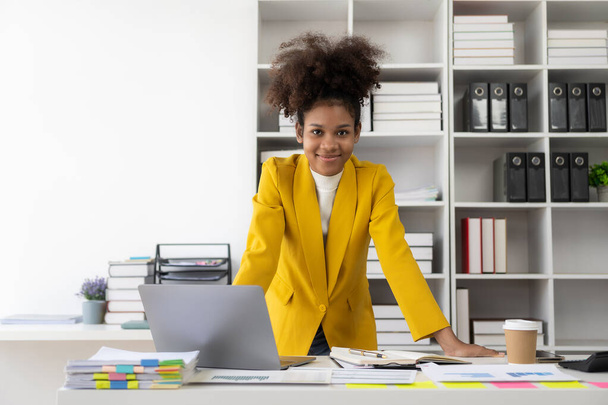 Donna d'affari afroamericana che lavora con laptop Grafici e grafici finanziari controllano i dati nei documenti cartacei al tavolo in ufficio - Foto, immagini