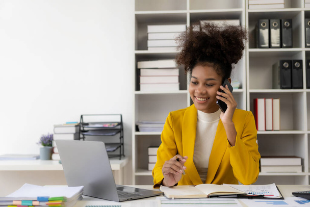 Афроамериканская деловая женщина, работающая с ноутбуками Финансовые диаграммы и графики проверяют данные в бумажных документах за столом в офисе - Фото, изображение