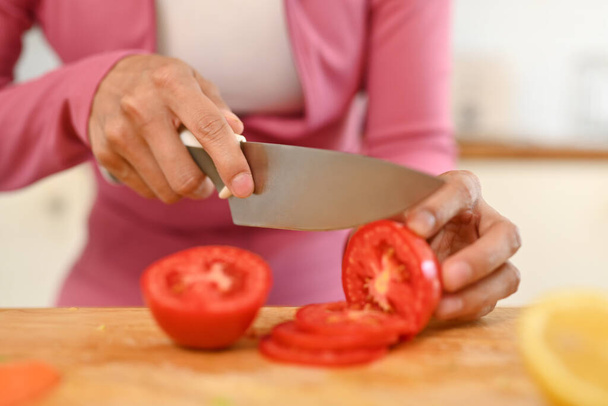 女性はナイフでトマトを切って,キッチンで健康的な朝食を準備します. 健康食品コンセプト. - 写真・画像