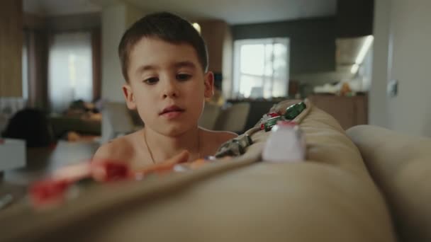 Хлопчик грає з різнокольоровими іграшковими машинами, сидячи на дивані у вітальні. Іграшкові автомобілі. Хлопчик, що вийшов. Щаслива сімейна концепція. - Кадри, відео