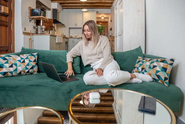 Mulher caucasiana sentada no sofá e trabalhando em projeto remoto no laptop na elegante sala de estar em casa - Foto, Imagem