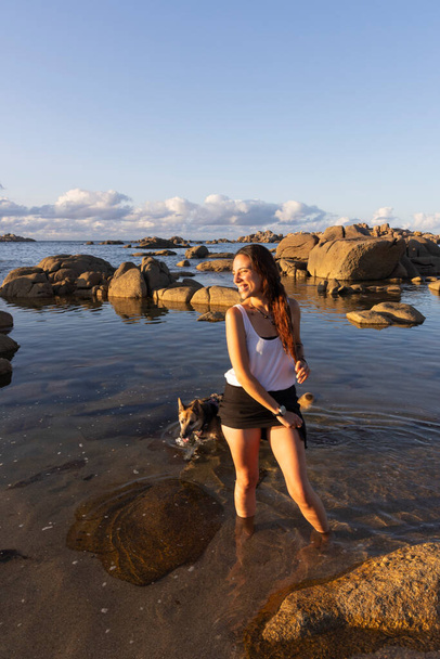 молода латинка на пляжі грає з собакою у воді на заході сонця - Фото, зображення