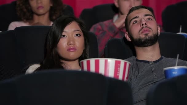映画館で幸せなカップル。映画館で映画を見ている陽気な若いカップル。映画、エンターテイメント、人々のコンセプト - 映画館で映画を見て幸せな友人。カップルと他の人が食べる - 映像、動画