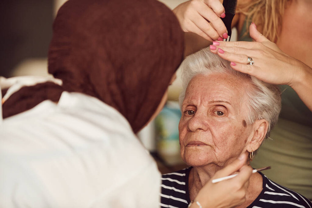 V této srdcervoucí reálné scéně, dívka v hidžábu a její sestra láskyplně nanášejí make-up na jejich starší babičku, připravují ji na speciální oslavu rodinného výročí, předvádění - Fotografie, Obrázek