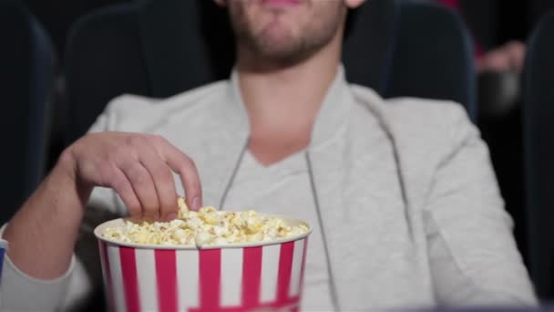 映画館で映画を見ているカップルは、ポップコーンを食べています。映画、エンターテイメント、人々のコンセプト - 映画館で映画を見て幸せな友人。カップルや他の人々はポップコーンを食べて飲む - 映像、動画