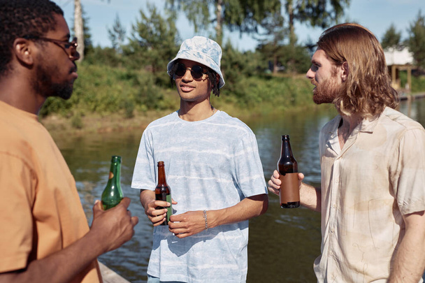 Ritratto in vita di tre giovani uomini che bevono birra all'aperto e chattano in estate - Foto, immagini