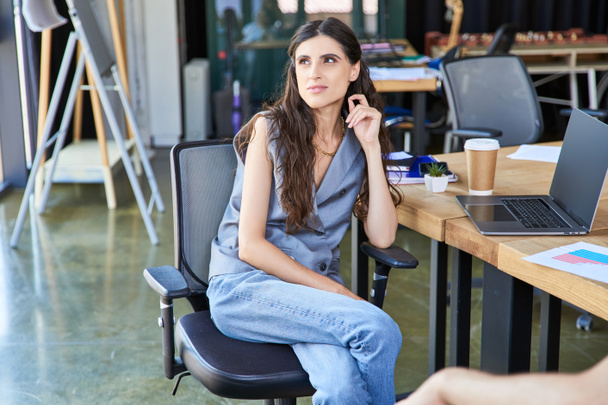 вдумлива бізнес-леді в повсякденному вбранні, сидячи і дивлячись далеко біля ноутбука і кави, щоб піти - Фото, зображення