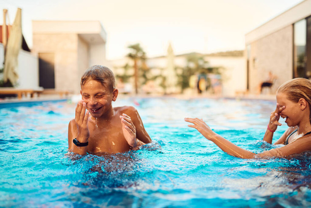 En una villa moderna iluminada por el sol, un hermano y una hermana jóvenes chapotean y juegan en la piscina, disfrutando del calor de un día de verano perfecto..  - Foto, Imagen