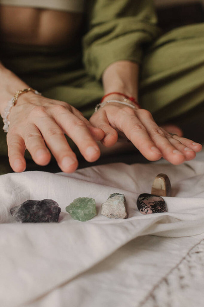 Woman holds jewelry made of natural stones in her hand, her hands are decorated with rings and bracelets. Handicrafts and creativity. Spirituality, religion, God concept. - Photo, Image