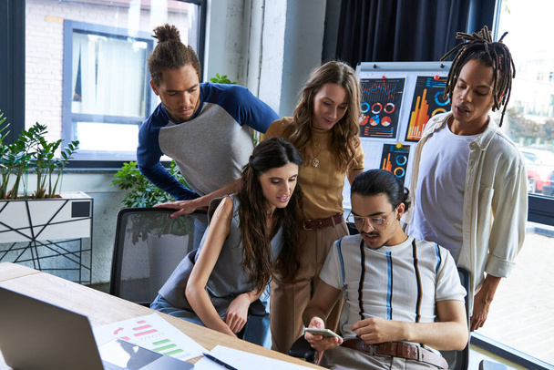 menedzser ül okostelefon közelében laptop és többnemzetiségű kreatív csapat irodai, startup koncepció - Fotó, kép