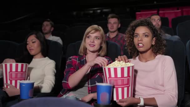 多重映画館に座って、映画を見て、ポップコーンを食べる若者のグループ。映画、エンターテイメント、人々のコンセプト - 映画館で映画を見て幸せな友人。カップルと他の人 - 映像、動画