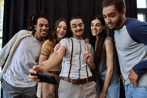 man in bril met overwinningsteken en foto 's maken op smartphone met gelukkig multi-etnisch team - Foto, afbeelding