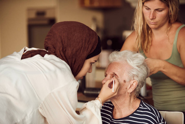 В этой трогательной реальной сцене девушка в хиджабе и ее сестра с любовью наносят макияж своей пожилой бабушке, готовят ее к особому празднованию годовщины семьи, демонстрируют - Фото, изображение