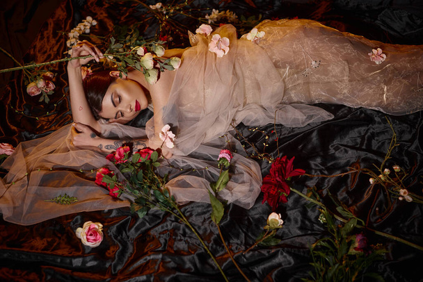 привлекательная и чувственная молодая женщина в романтическом прозрачном платье, лежащем среди цветущих цветов - Фото, изображение