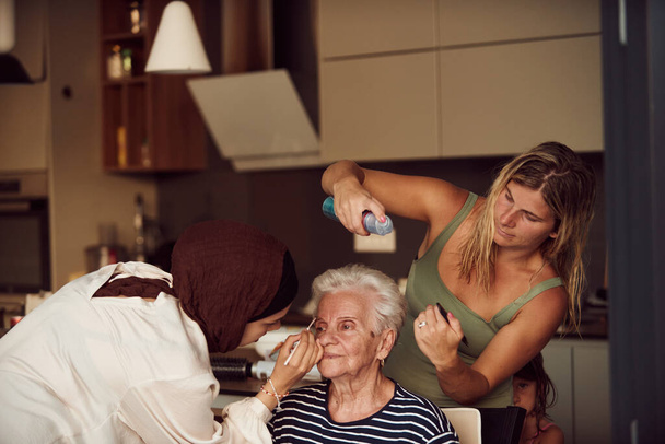 Nesta cena emocionante da vida real, uma menina em um hijab e sua irmã amorosamente aplicar maquiagem para sua avó idosa, preparando-a para uma celebração especial do aniversário da família, mostrando o - Foto, Imagem