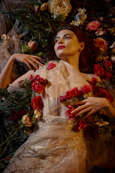 θηλυκή κομψότητα, τρυπημένη νεαρή γυναίκα σε ρομαντικό διάφανο φόρεμα που βρίσκεται ανάμεσα σε όμορφα λουλούδια - Φωτογραφία, εικόνα