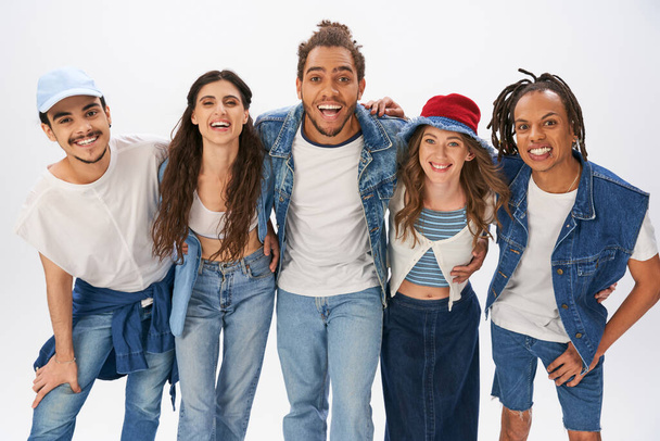 Unbekümmerte multikulturelle Freunde in angesagter Streetwear umarmen und lächeln in die Kamera auf grau - Foto, Bild