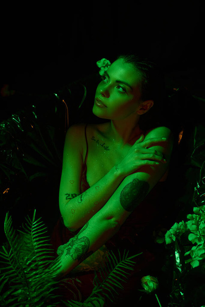 luz verde, mujer joven atractiva con el pelo mojado posando en la bañera entre flores, cuerpo mojado - Foto, Imagen