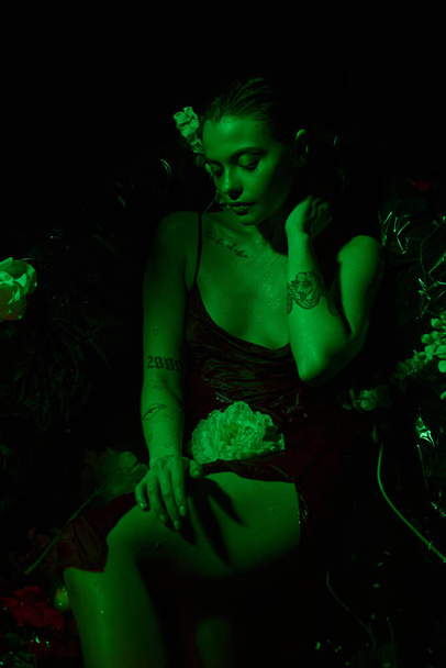 Yeşil ışık, küvette çiçeklerin arasında poz veren ıslak saçlı çekici genç kadın manzarası. - Fotoğraf, Görsel