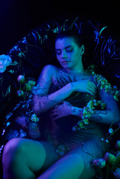 top view, young woman with wet hair diving into water in bathtub with flowers with blue light - Photo, Image
