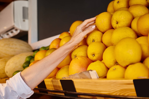 abgeschnittene Ansicht der Hand einer reifen fröhlichen Frau beim Orangenpflücken im Lebensmittelgeschäft, Bauernmarkt - Foto, Bild