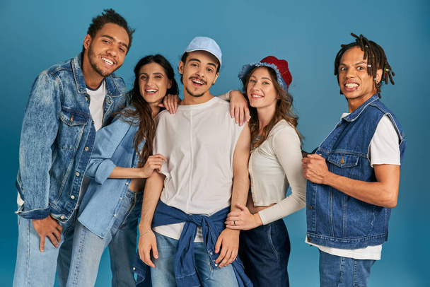 різноманітна група збуджених міжрасових друзів в модному і джинсовому одязі, дивлячись на камеру на синьому - Фото, зображення