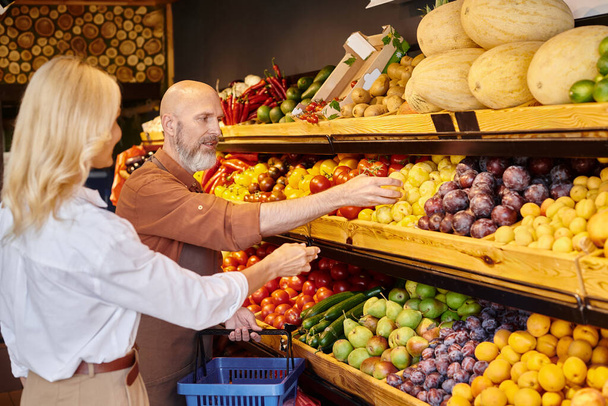 centrarse en el vendedor maduro barbudo ayudar a su cliente mayor borrosa para elegir frutas - Foto, imagen