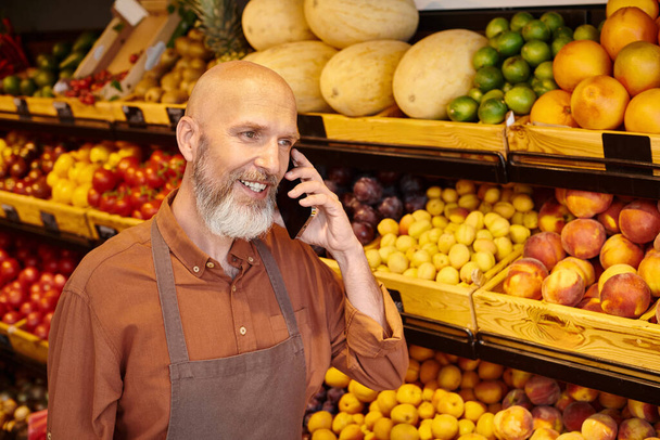 dojrzały dobrze wyglądający sprzedawca z brodą rozmawiający przez telefon podczas przerwy od pracy w sklepie spożywczym - Zdjęcie, obraz