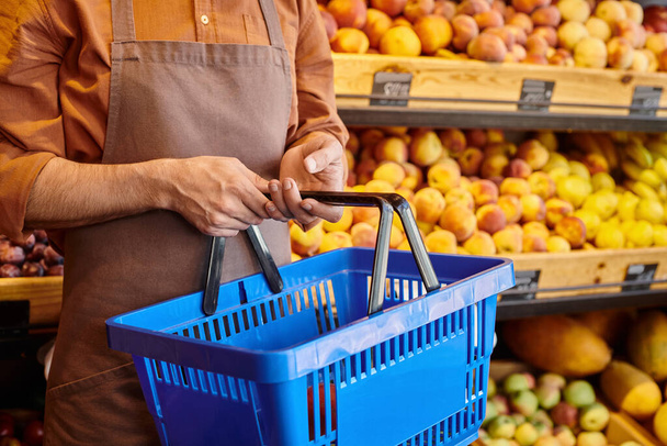 Arka planda bulanık meyvelerle elinde alışveriş sepeti tutan olgun bir pazarlamacı görüntüsü. - Fotoğraf, Görsel