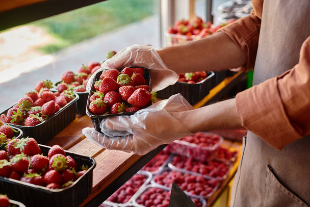 καλλιεργημένη άποψη του ώριμου πωλητή κρατώντας πακέτο φρέσκες ζωντανές φράουλες στα χέρια στο μανάβικο - Φωτογραφία, εικόνα