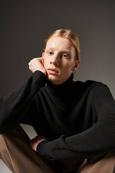 vertical shot of young non binary model sitting on floor with crossed legs and looking at camera - Fotoğraf, Görsel