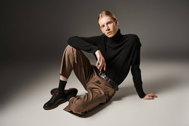 young non binary person in black turtleneck sitting on floor and looking at camera, fashion concept - Photo, Image