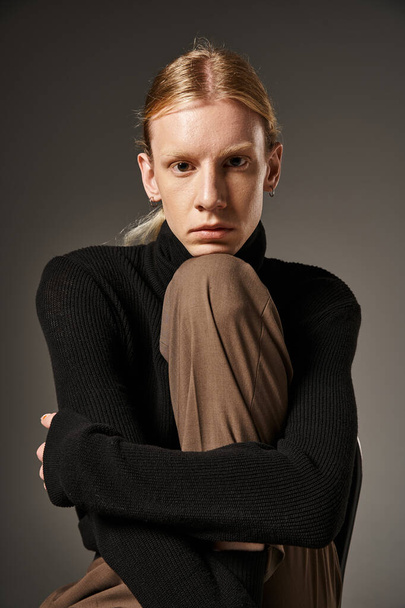 young attractive non binary person with ponytail and black turtleneck posing and looking at camera - Photo, Image