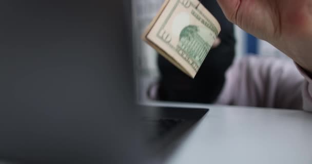 Cybercriminel en masque noir tient des dollars sur crochet et regarde dans l'ordinateur portable. Escrocs de réseau et concept d'arnaque - Séquence, vidéo