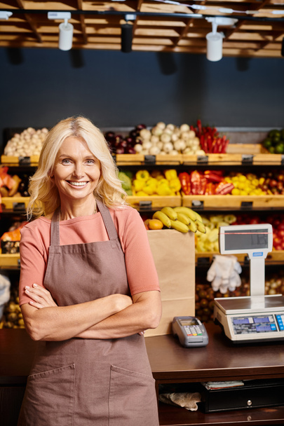 joyous blonde mature saleswoman posing with arms crossed on chest and smiling happily at camera - Photo, Image