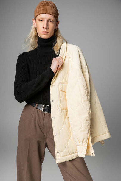 bel modello non binario in posa con elegante giacca invernale sulla spalla e guardando la fotocamera - Foto, immagini
